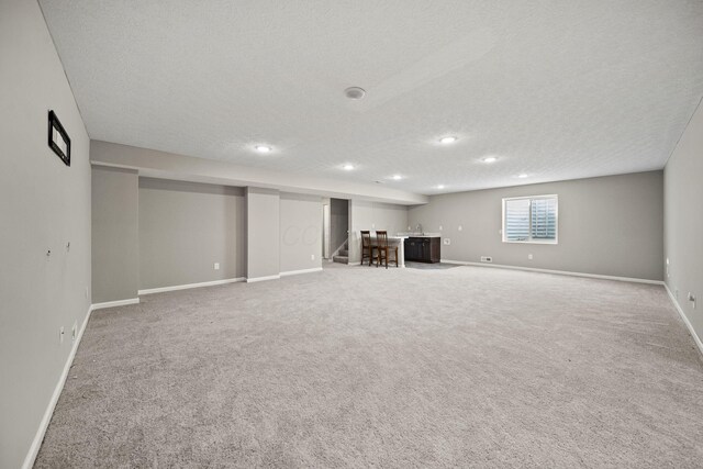basement featuring a textured ceiling, light colored carpet, baseboards, indoor wet bar, and recessed lighting