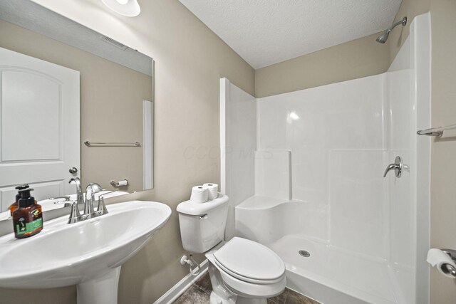 bathroom with walk in shower, a sink, toilet, a textured ceiling, and baseboards