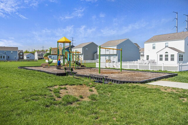 communal playground featuring a lawn, fence, and a residential view
