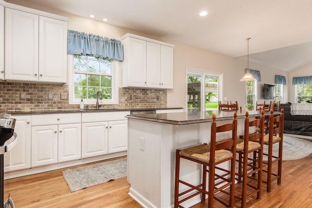 kitchen featuring a sink, light wood-style floors, a kitchen breakfast bar, white cabinetry, and backsplash