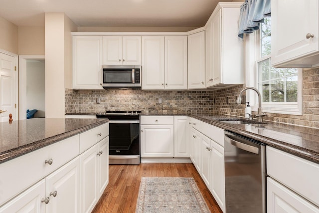 kitchen featuring white cabinets, appliances with stainless steel finishes, a sink, light wood-style floors, and dark stone counters