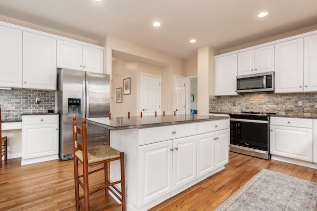 kitchen with decorative backsplash, a kitchen island, white cabinetry, light wood finished floors, and appliances with stainless steel finishes