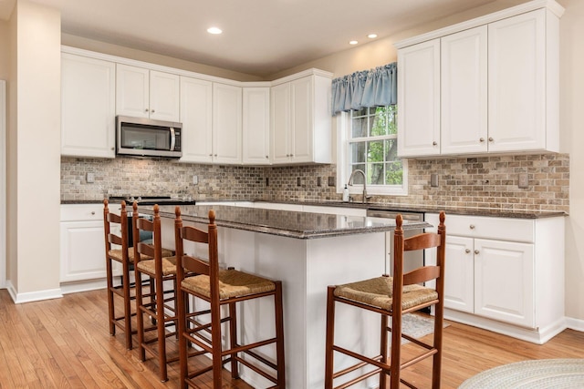 kitchen with white cabinets, stainless steel microwave, a breakfast bar, and light wood-type flooring