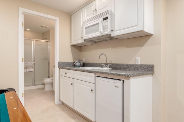 kitchen featuring visible vents, fridge, white microwave, white cabinets, and a sink