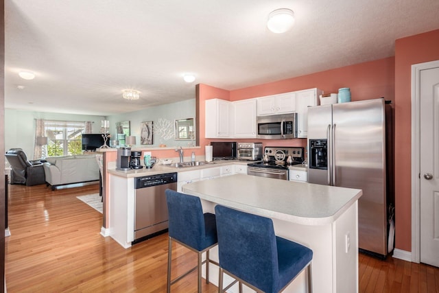 kitchen with appliances with stainless steel finishes, a sink, light countertops, light wood-style flooring, and a peninsula