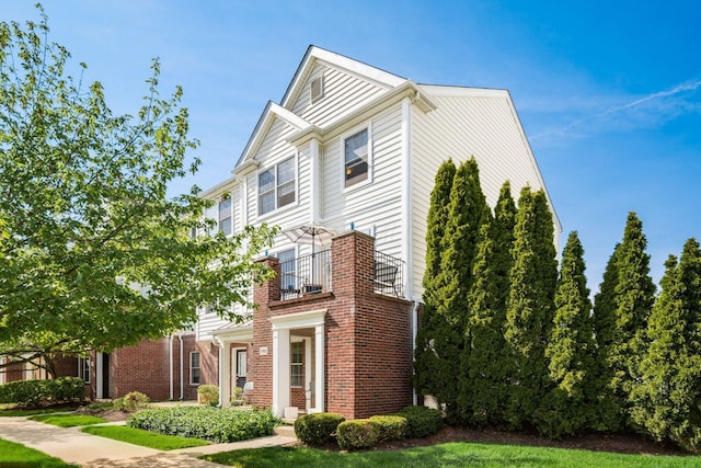 view of front of property with brick siding, a balcony, and a front yard