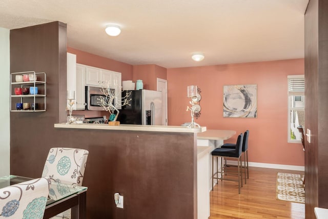 kitchen featuring a peninsula, light wood-style floors, a breakfast bar area, white cabinets, and appliances with stainless steel finishes