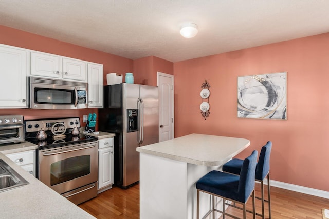 kitchen featuring a breakfast bar area, light countertops, white cabinetry, light wood-style flooring, and appliances with stainless steel finishes