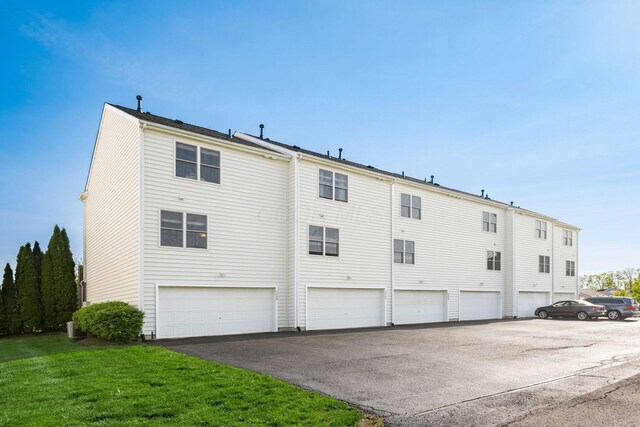rear view of property featuring a lawn, an attached garage, and driveway
