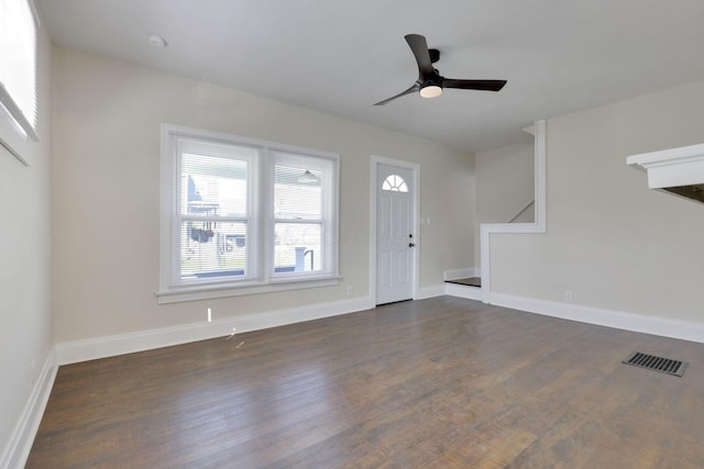 unfurnished living room featuring a ceiling fan, dark wood-style flooring, visible vents, baseboards, and stairs