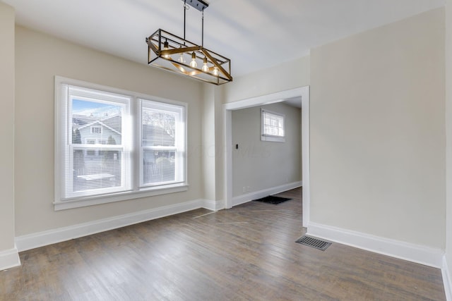 unfurnished dining area featuring visible vents, baseboards, wood finished floors, and a chandelier