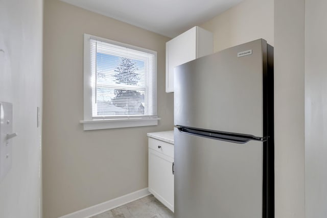 kitchen featuring light countertops, baseboards, freestanding refrigerator, and white cabinetry