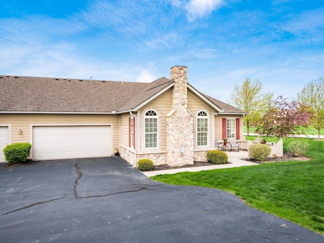 view of front facade featuring a front lawn, stone siding, a chimney, an attached garage, and driveway