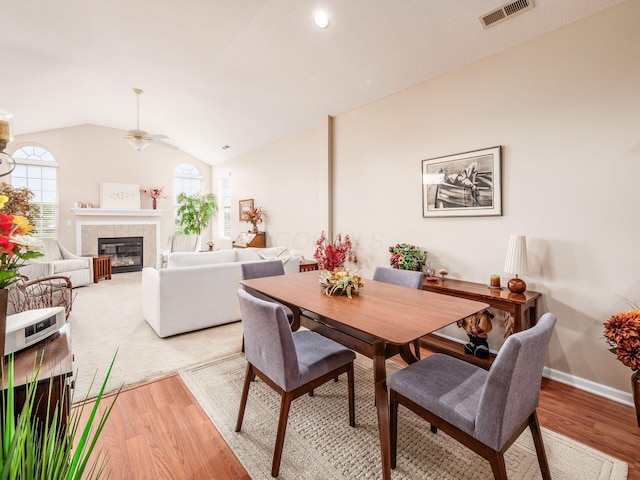 dining area with visible vents, ceiling fan, a tiled fireplace, and light wood-type flooring