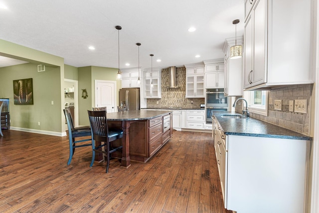 kitchen with glass insert cabinets, wall chimney range hood, dark wood-type flooring, a sink, and stainless steel appliances