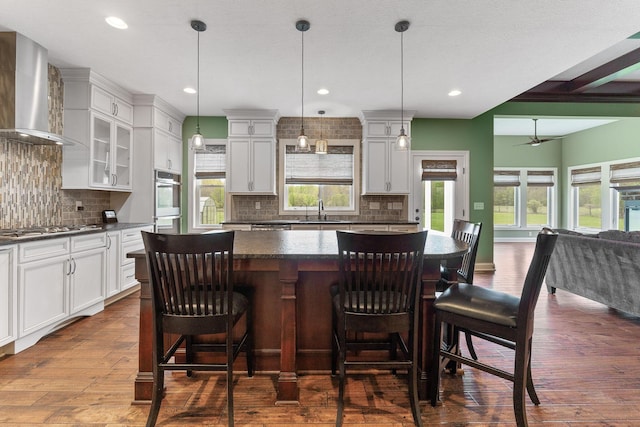 kitchen featuring wall chimney range hood, dark countertops, dark wood finished floors, a center island, and tasteful backsplash