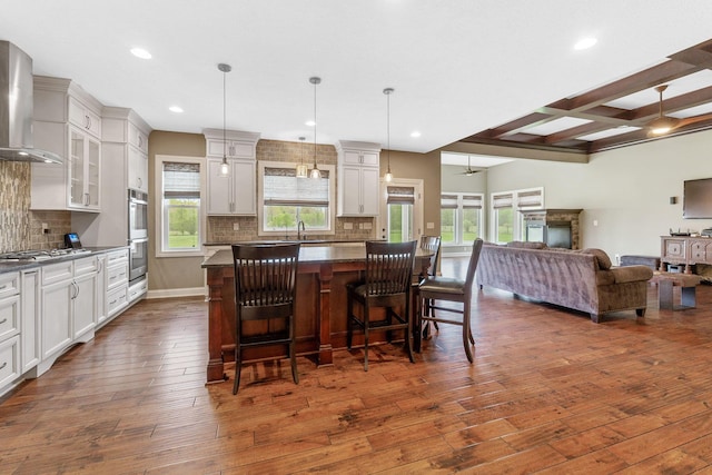 kitchen featuring wall chimney range hood, dark countertops, appliances with stainless steel finishes, dark wood-style floors, and open floor plan