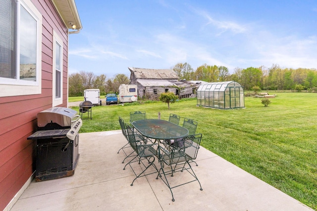 view of patio with grilling area, a greenhouse, an outdoor structure, and outdoor dining space