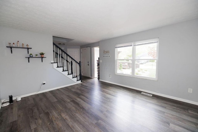 unfurnished living room with dark wood finished floors, baseboards, stairs, and visible vents