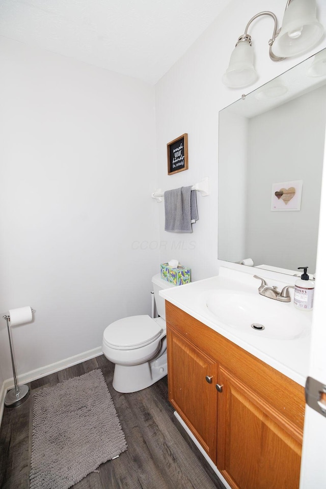 half bathroom featuring vanity, baseboards, toilet, and wood finished floors