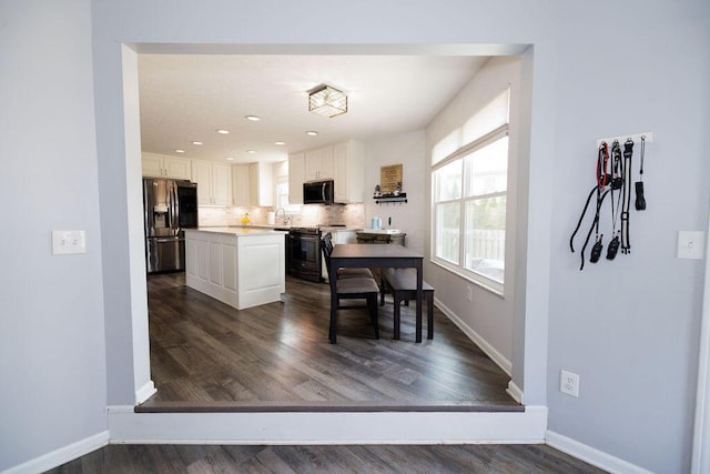 kitchen with white cabinets, stove, baseboards, fridge with ice dispenser, and a kitchen island