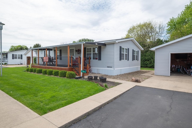 manufactured / mobile home with covered porch, an outbuilding, a garage, aphalt driveway, and a front lawn
