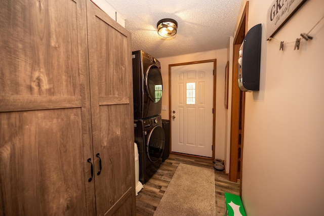 clothes washing area with laundry area, stacked washer and clothes dryer, a textured ceiling, and dark wood-type flooring