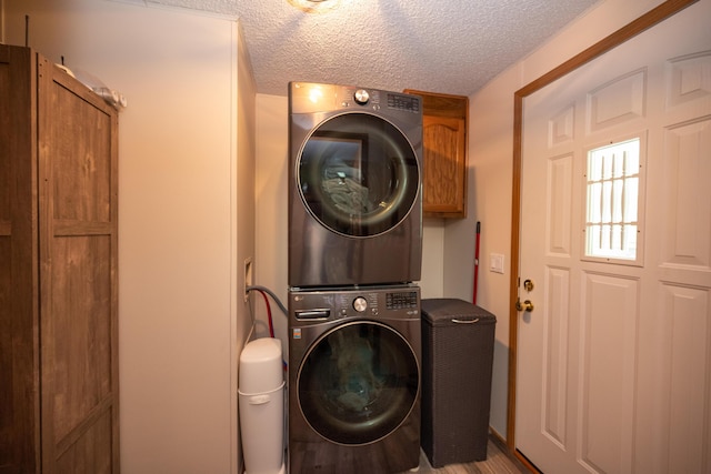 laundry area with a textured ceiling, stacked washer and clothes dryer, and cabinet space