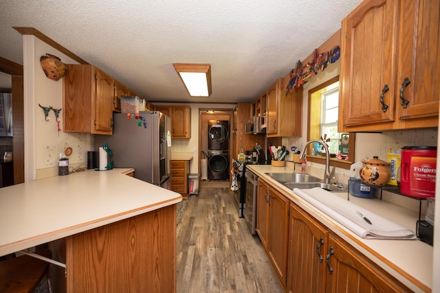 kitchen featuring stacked washer / drying machine, wood finished floors, a sink, light countertops, and stainless steel fridge