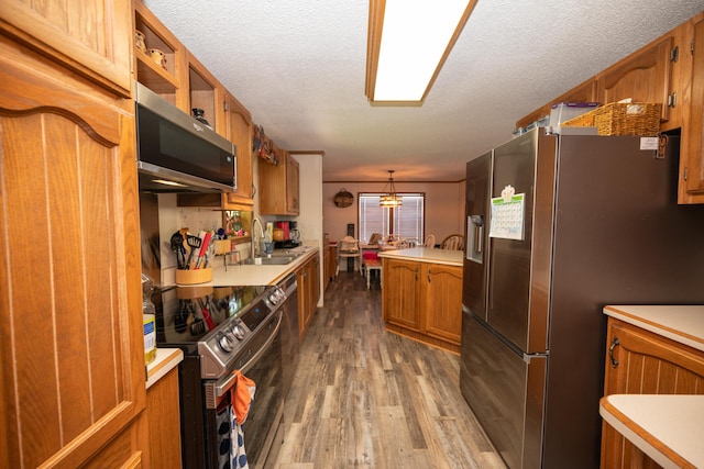 kitchen featuring appliances with stainless steel finishes, a sink, light countertops, brown cabinetry, and wood finished floors
