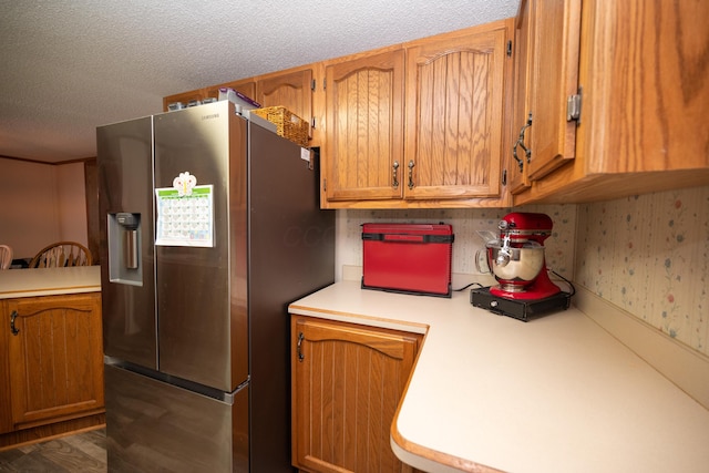 kitchen with brown cabinetry, wood finished floors, stainless steel fridge, light countertops, and a textured ceiling