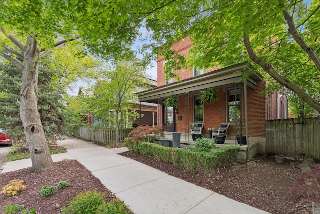 view of front facade with covered porch, brick siding, and fence
