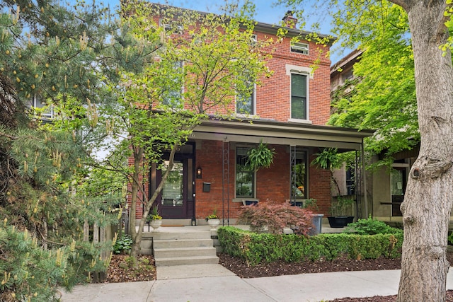 italianate-style house featuring covered porch, a chimney, and brick siding