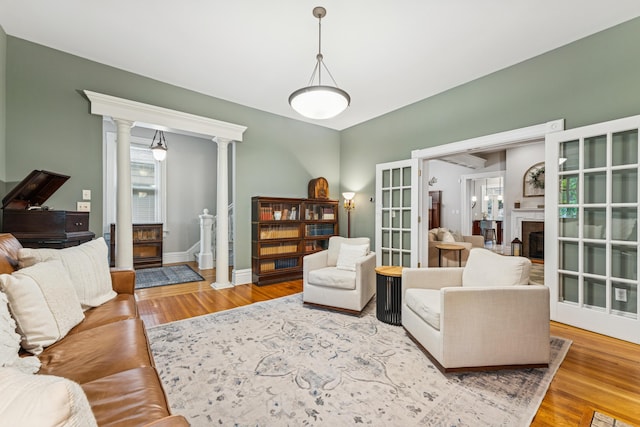 living room featuring baseboards, a fireplace, ornate columns, and wood finished floors