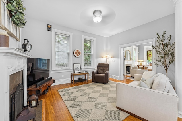 living area with light wood-style floors, baseboards, ceiling fan, and a fireplace