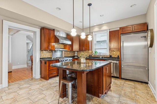 kitchen with wall chimney range hood, stone finish flooring, baseboards, and appliances with stainless steel finishes