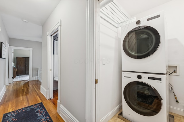 washroom featuring stacked washer / drying machine, baseboards, laundry area, and light wood-type flooring