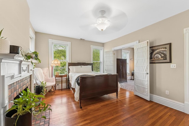 bedroom with wood-type flooring, baseboards, ceiling fan, and a brick fireplace