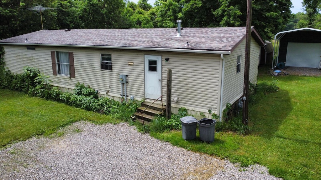 view of front of home with entry steps, a carport, a shingled roof, and a front yard
