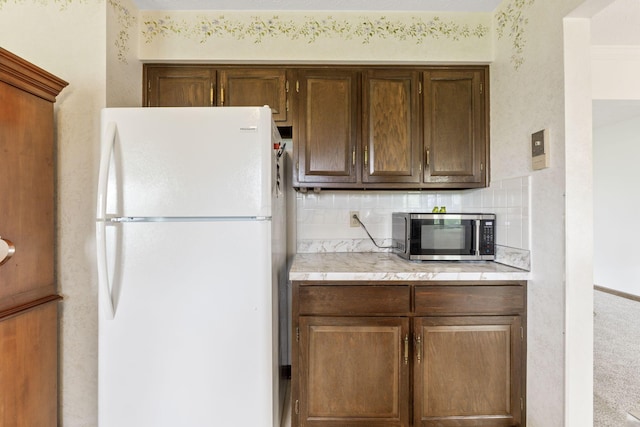 kitchen with stainless steel microwave, freestanding refrigerator, decorative backsplash, and light countertops