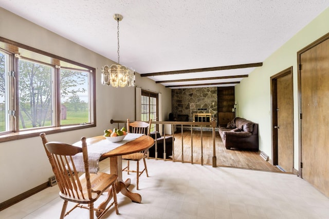 dining area featuring a stone fireplace, an inviting chandelier, beam ceiling, and a textured ceiling