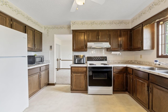 kitchen with a sink, freestanding refrigerator, range with electric cooktop, stainless steel microwave, and under cabinet range hood