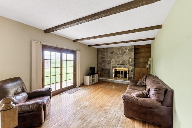 living area with light wood-style floors, a stone fireplace, and beam ceiling