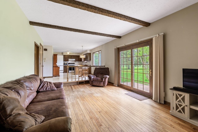 living area featuring light wood finished floors, a textured ceiling, visible vents, and beamed ceiling