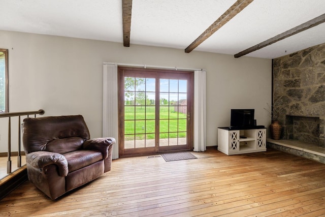 living area featuring beamed ceiling, hardwood / wood-style floors, and a fireplace