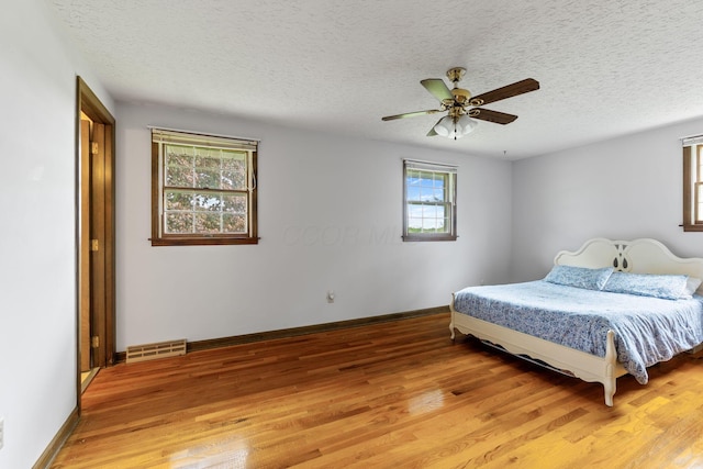 bedroom with ceiling fan, a textured ceiling, light wood-style flooring, and visible vents