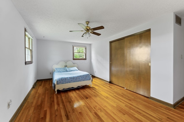 bedroom with a textured ceiling, baseboards, ceiling fan, visible vents, and light wood-type flooring
