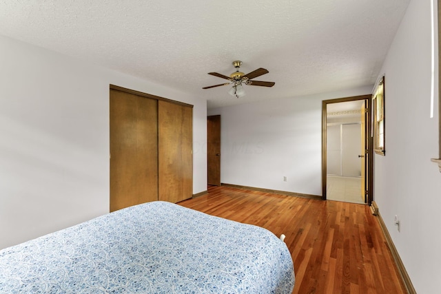 bedroom with a ceiling fan, a closet, light wood-style flooring, a textured ceiling, and baseboards