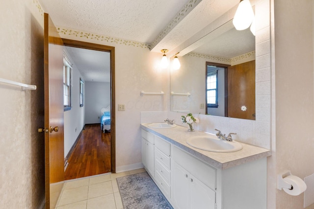 full bath with a sink, double vanity, a textured ceiling, and tile patterned flooring