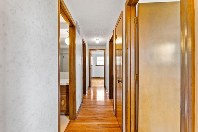 corridor featuring a textured ceiling, light wood-style flooring, and a textured wall